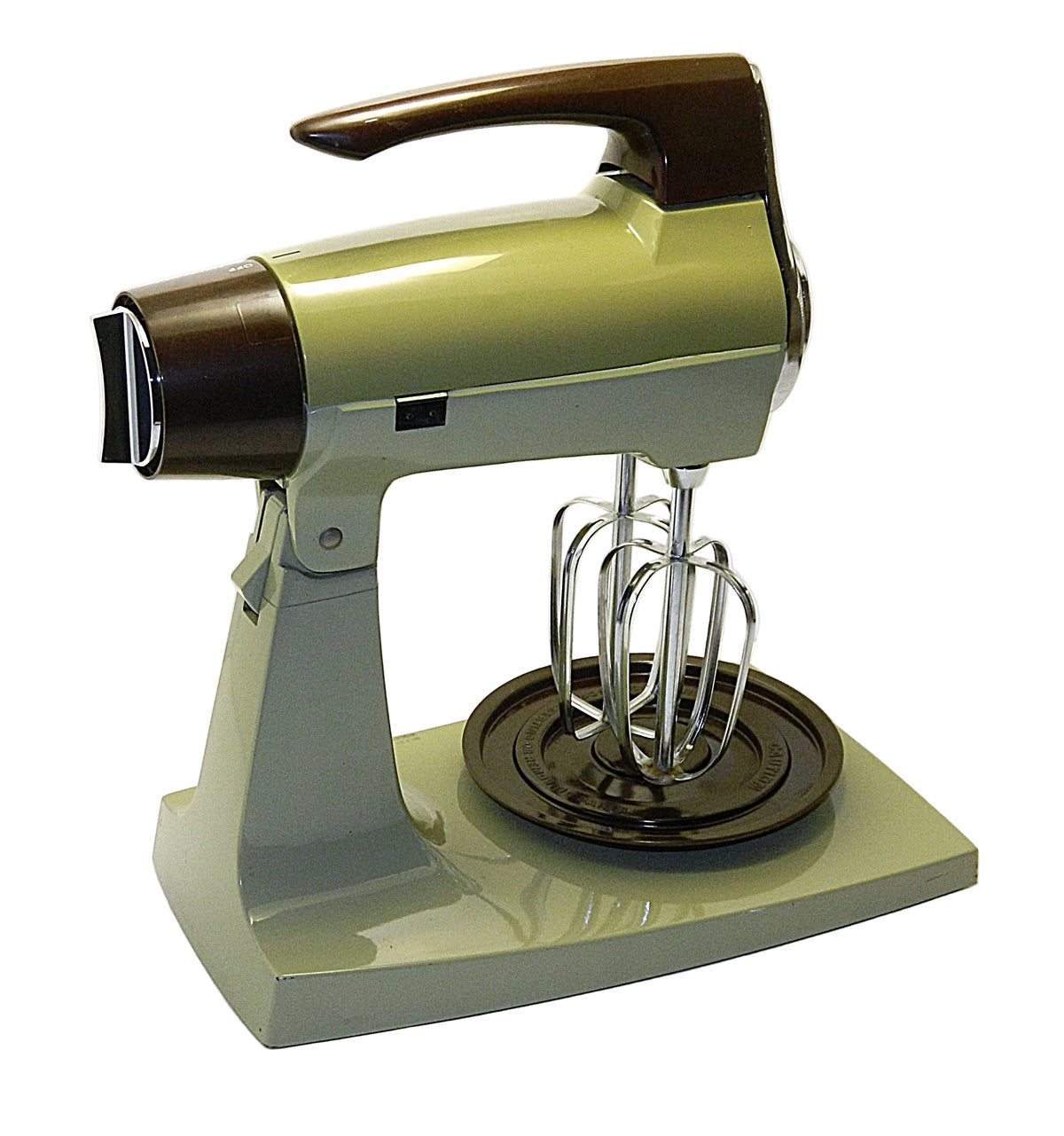 A vintage-style stand mixer with a glossy olive green body and dark brown accents, featuring a metal wire whisk attachment and a round mixing tray, photographed on a plain white studio background.