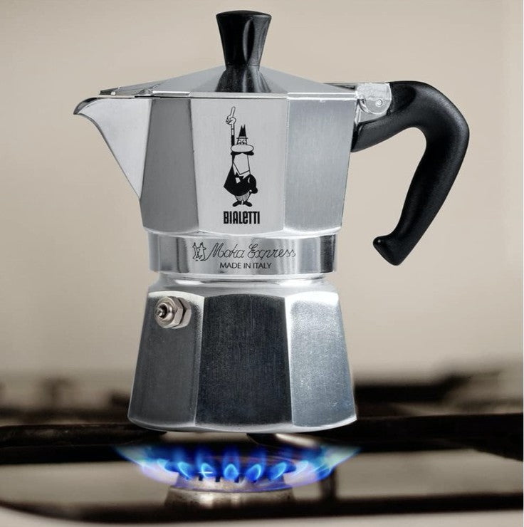 Stainless steel Moka Express coffee maker on a stove with a blurred background